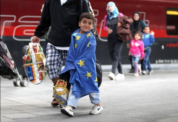 طفل مع أبيه يلف جسمه بعلم الاتحاد الأوربي بعد وصوله الي ألمانيا