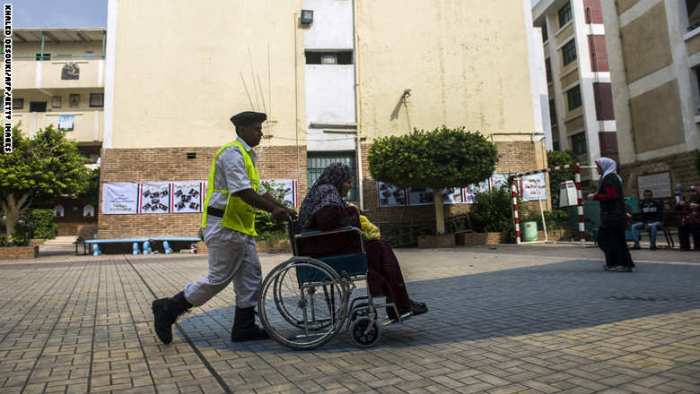 رجل شرطة يساعد احدي السيدات علي كرسي متحرك بأحد اللجان الإنتخابية
