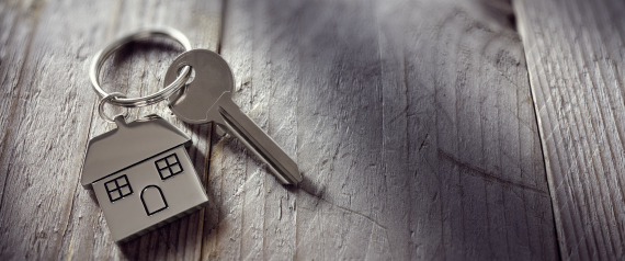 House key on a house shaped keychain resting on wooden floorboards concept for real estate, moving home or renting property