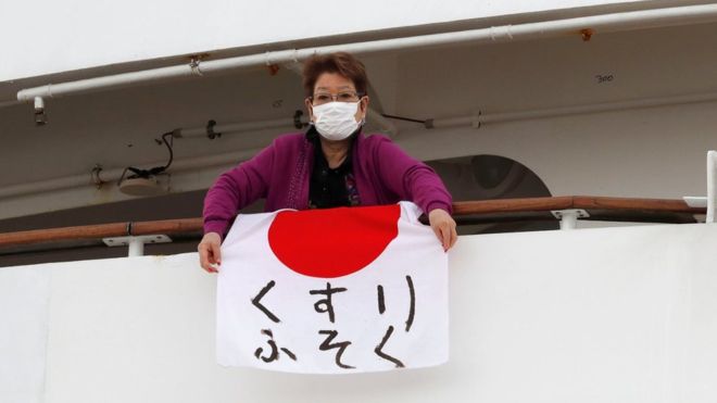 أحدي المسافرات علي سفينة أميرة الألماس تمسك بالعلم الياباني وتضع كمامة خوفا من وصول الفيروس المتفشي في السفينة إليها