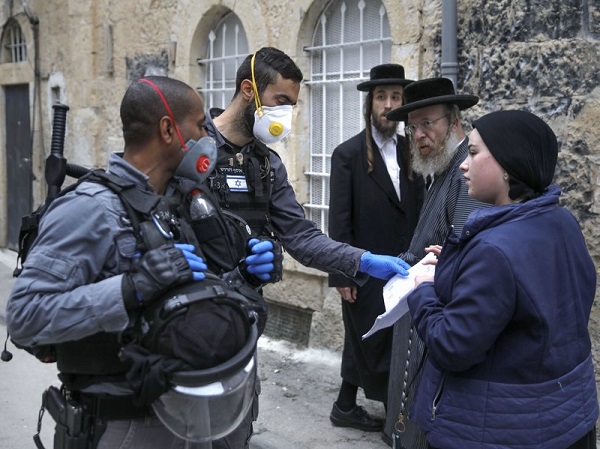 ضباط شرطة إسرائيليون يرتدون قفازات واقية وأقنعة يفحصون الأوراق وهم يفرضون قيودًا في حي يهودي متشدد في القدس يوم الثلاثاء 31 مارس، خلال إغلاق جزئي للحد من انتشار عدوى فيروسات كورونا