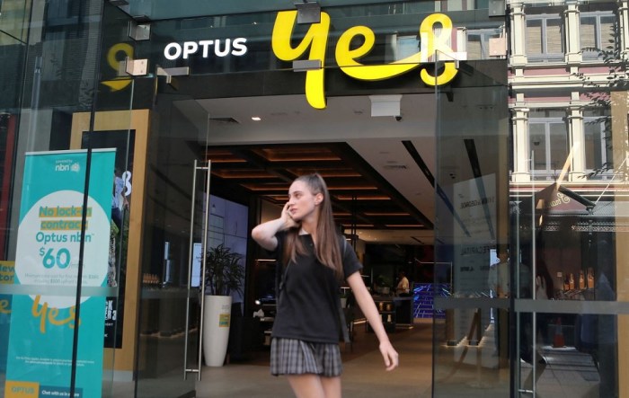 امرأة تستخدم هاتفها المحمول وهي تمشي أمام متجر Optus في سيدني، أستراليا 