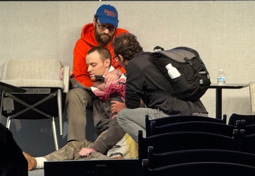 ريتشارد كنيبل أحد أعضاء مؤتمر ويكيميديا، في الخلف، اندفع ليمسك برجل مسلح بعد أن قال شهود عيان إن الرجل هدد بإطلاق النار على نفسه في مؤتمر ويكيبيديا في مانهاتن يوم الجمعة 17 أكتوبر 2025